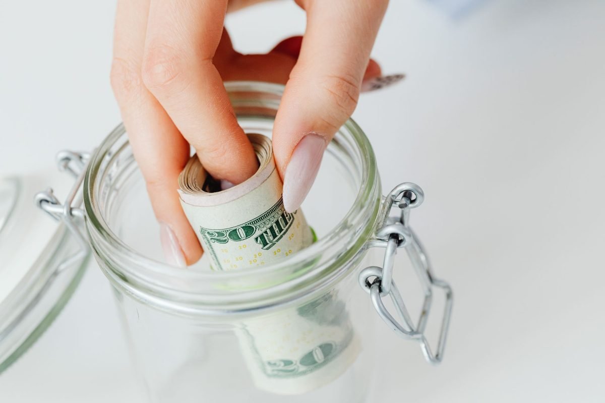 Person reviewing a household budget on a laptop while saving money in a glass jar